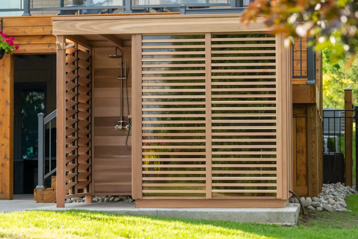 Pure Cube Outdoor Sauna with Shower in cedar, with a stainless rain shower and slatted privacy panels beside a backyard deck